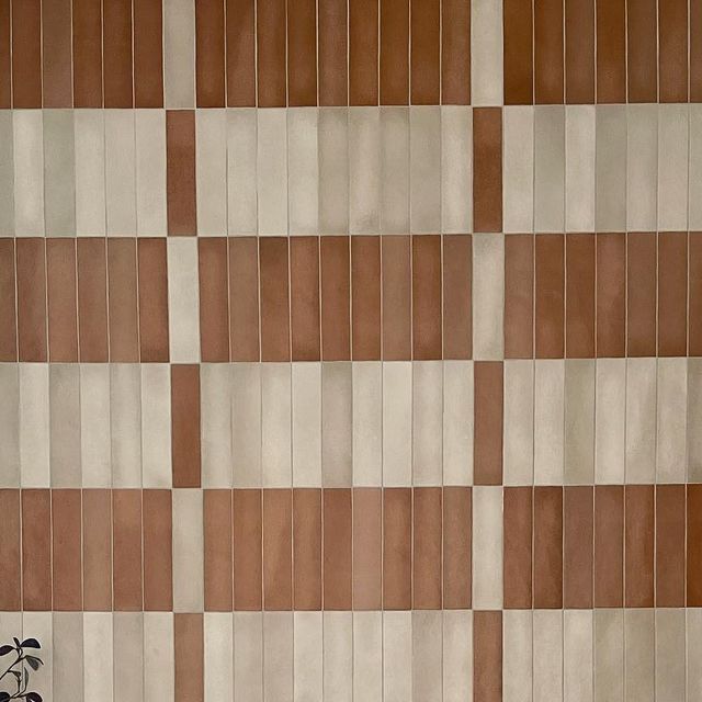 a brown and white checkered wall with a clock on it's side next to a plant