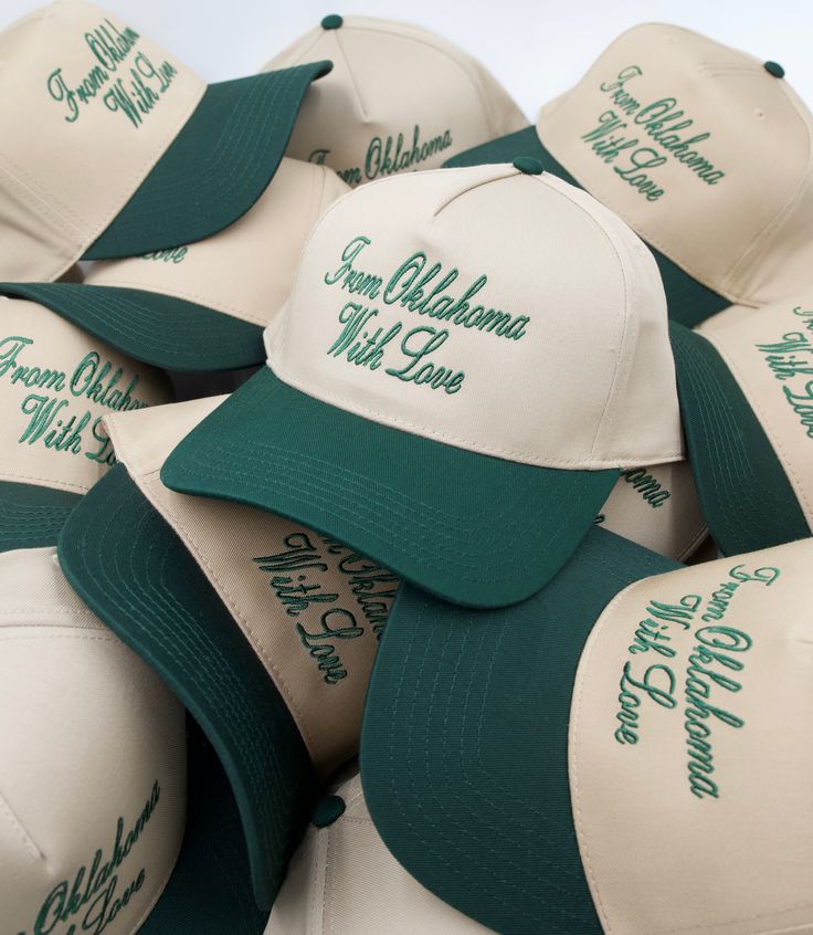 many hats with green lettering on them are stacked up in a pile and the caps have white brimmed visors