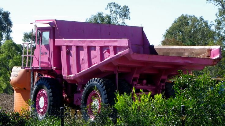 a pink dump truck is parked in the bushes