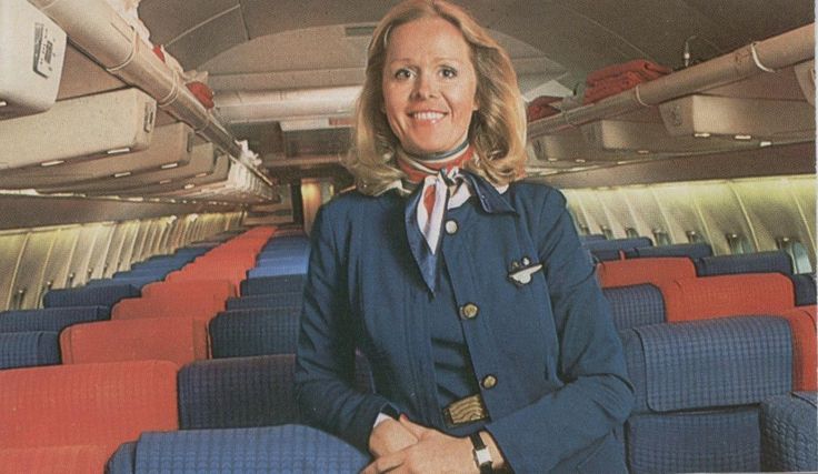 a woman in an airplane cabin with her hands on her hips and looking at the camera