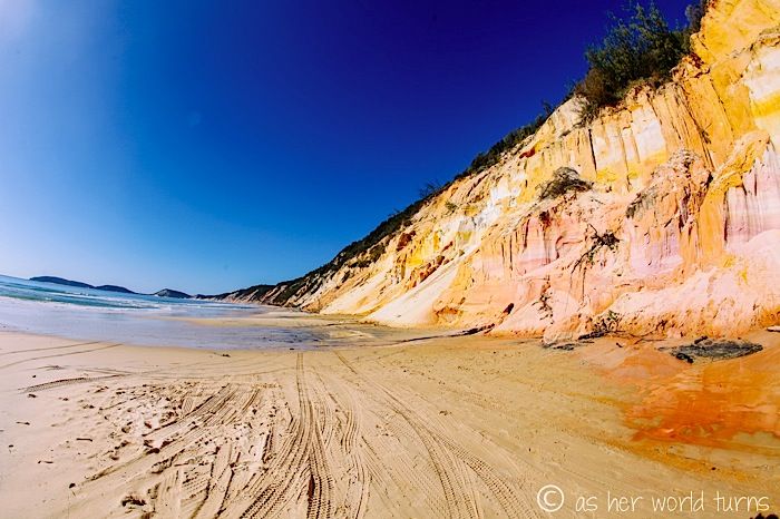 a sandy beach next to the ocean under a blue sky