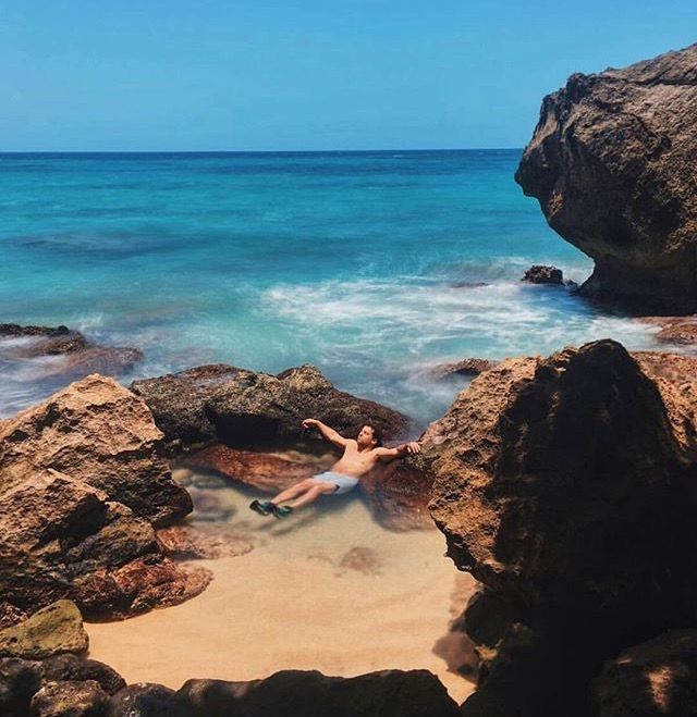 a woman laying on top of a sandy beach next to the ocean in front of rocks