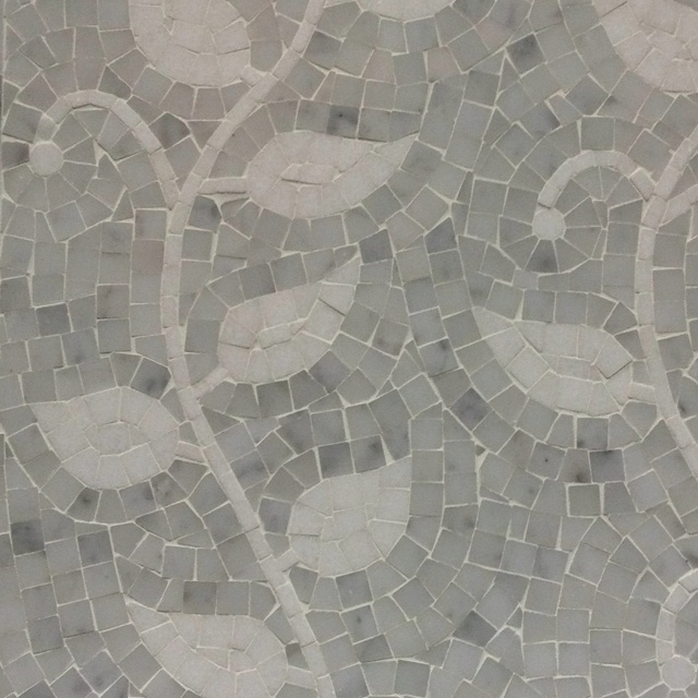 a close up view of a mosaic tile wall with flowers and leaves in grey tones