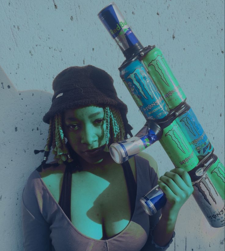 a woman with dreadlocks is holding two green cans and a blue bottle in her hand