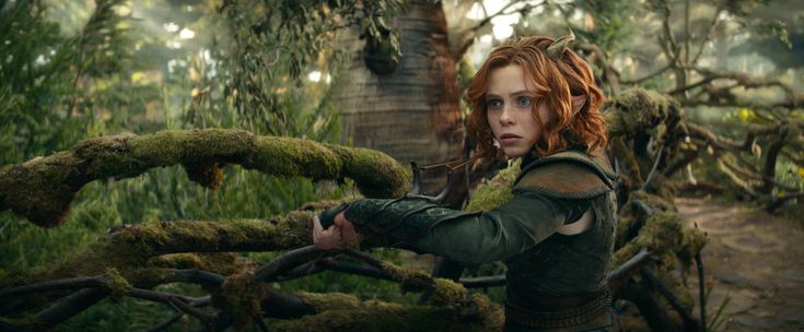 a woman with red hair is in the woods and holding onto a tree branch that has moss growing on it