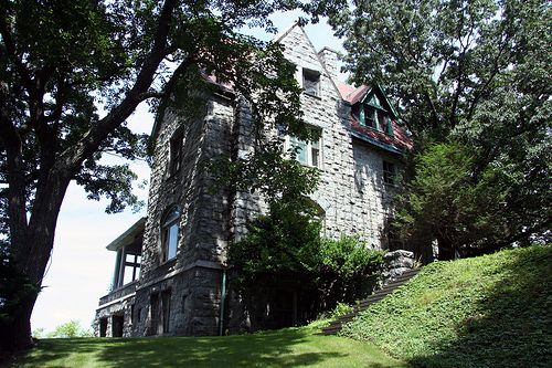 an old stone house sitting on top of a lush green hillside next to trees and bushes