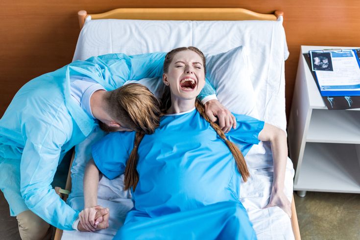 two women in blue gowns are laying on a hospital bed and one is holding her arm around the other