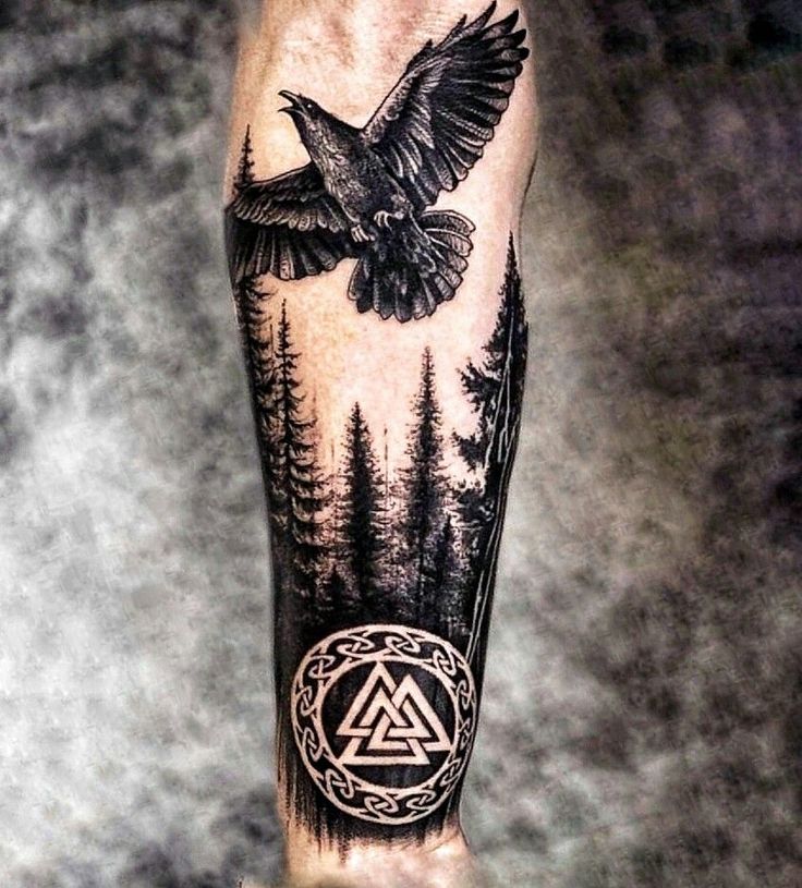 a man's arm with a bird and triangle tattoo on it, surrounded by trees