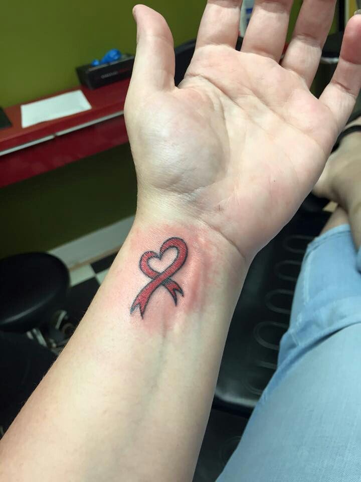 a woman's arm with a tattoo on it that has a red ribbon in the shape of a heart