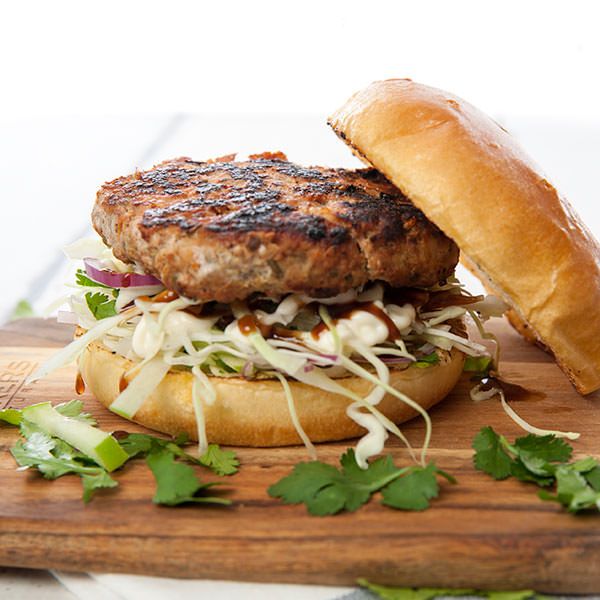 a burger with lettuce and cheese on a wooden cutting board next to a roll