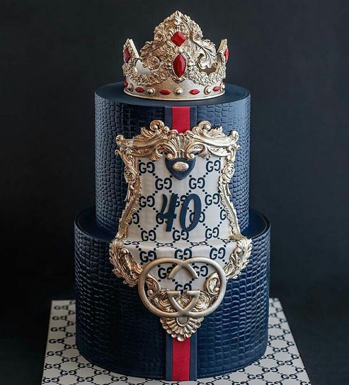 a three tiered cake decorated with blue and red ribbon, gold crown on top