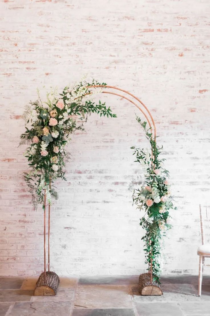 an arch decorated with flowers and greenery stands in front of a white brick wall