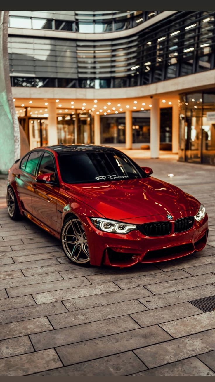 a red bmw car parked in front of a building with lights on it's windows