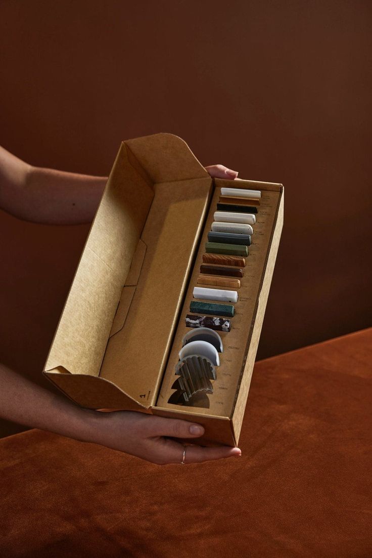 a person holding an open box with different items in it on top of a table