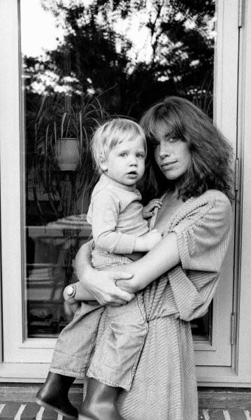 a woman holding a child in front of a window with her arms around her shoulders