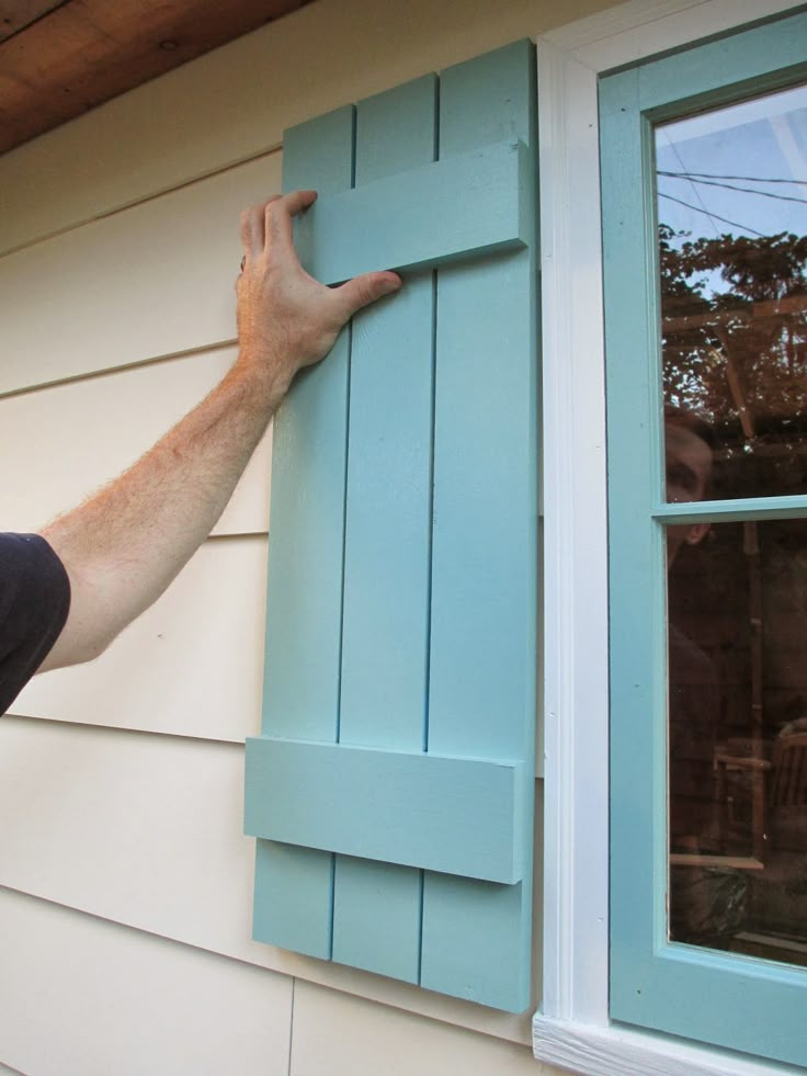 a man is painting the side of a house with blue shutters and a window