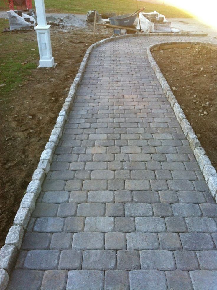 a brick walkway in the middle of a yard with grass and dirt on both sides