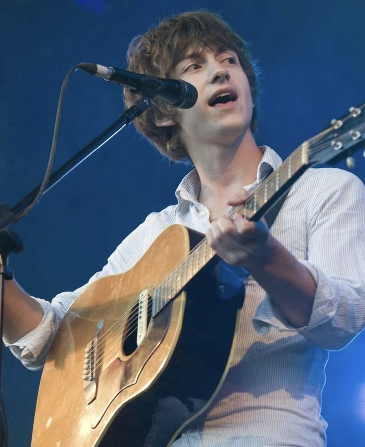 a young man holding a guitar while singing into a microphone