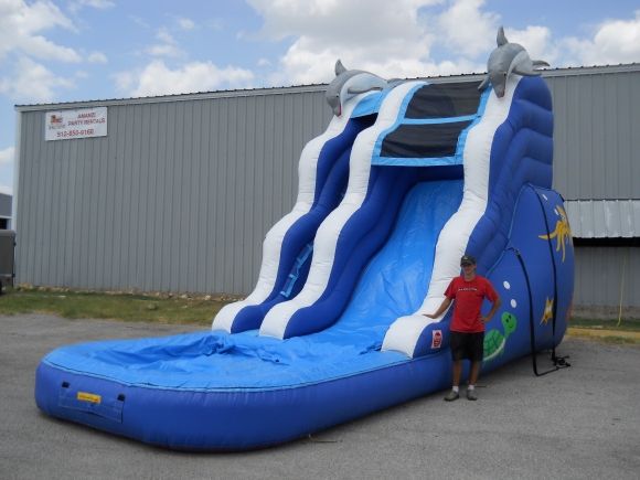 a man standing next to a blue and white inflatable slide with dolphins on it