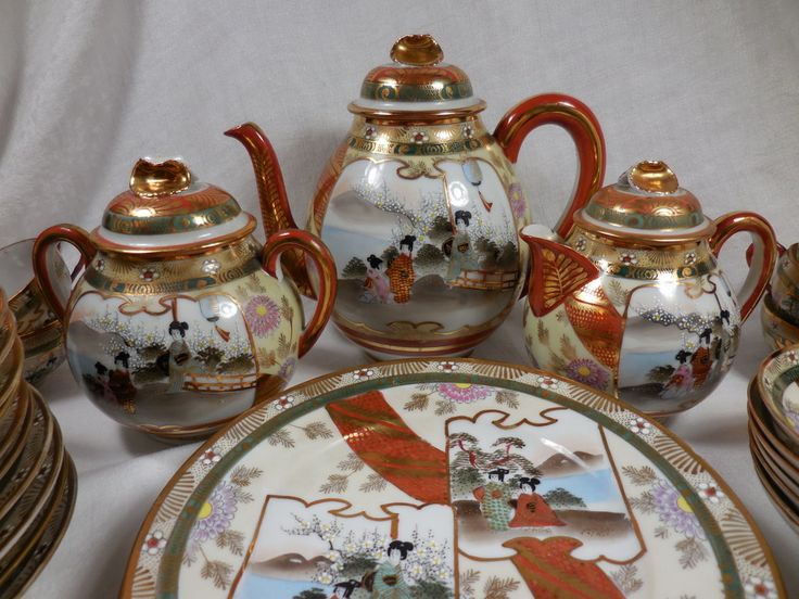 an assortment of porcelain teapots and plates on a white tablecloth with gold trim