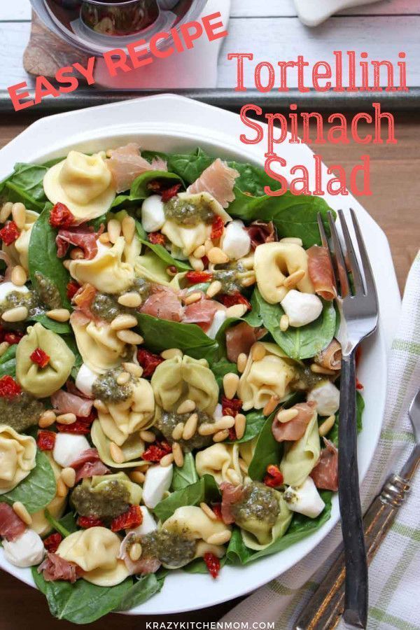 a white plate topped with tortellini spinach salad next to a glass of wine