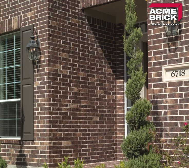 a brick building with green shutters and bushes in front of the window that says acme brick