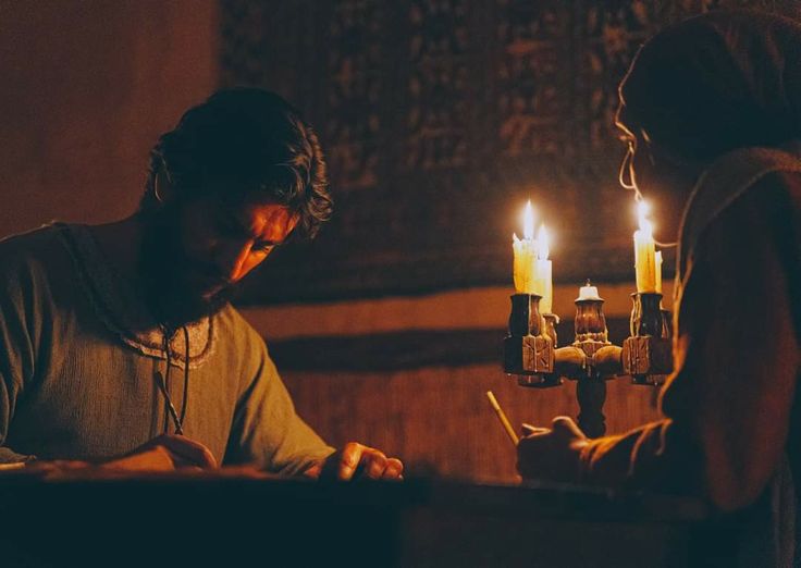 two people standing next to each other with candles in their hands and writing on paper