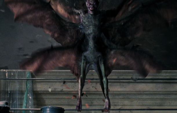 a demonic creature with its wings spread out in front of a man sitting on a chair