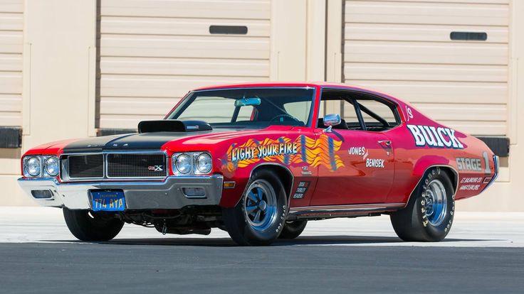 a red and black muscle car parked in front of a garage with the word buddy on it's side