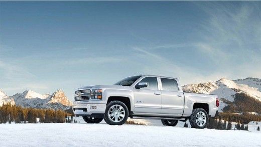 a silver truck parked in the middle of a snow covered field with mountains in the background