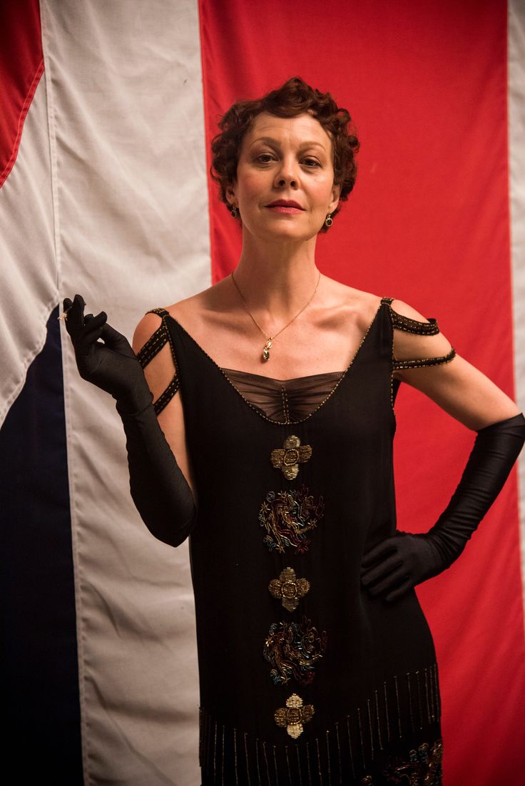 a woman standing in front of an american flag with her hands on her hips and wearing black gloves