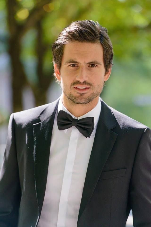 a man in a tuxedo and bow tie is looking at the camera while standing outside