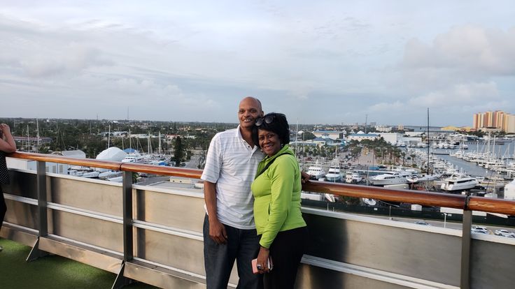 a man and woman standing next to each other on top of a building with boats in the background