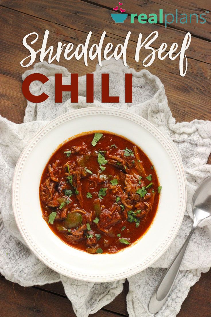 a white bowl filled with shredded beef chili on top of a table next to a spoon