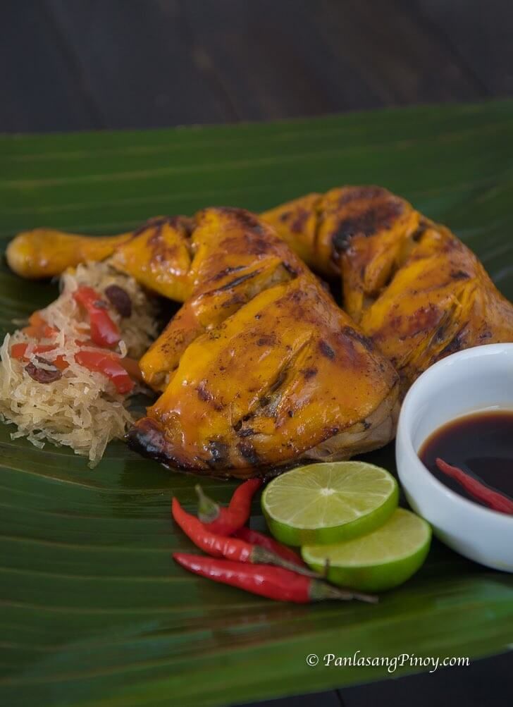 grilled chicken on a banana leaf next to some dipping sauce and sliced red peppers