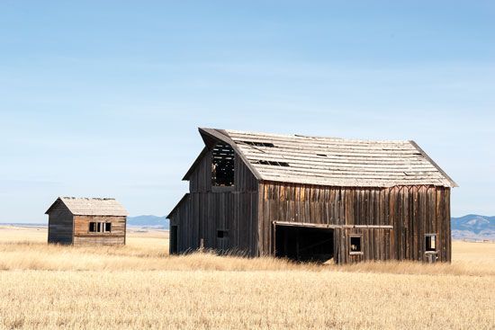 two old wooden barns in an open field