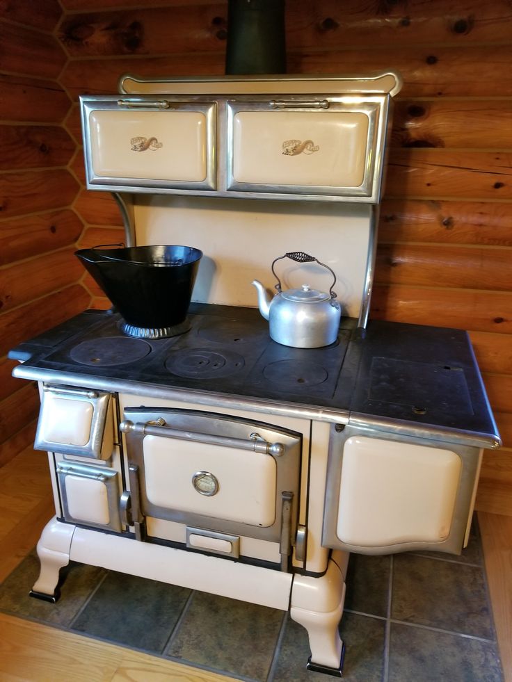 an old fashioned stove with a tea kettle on it's burner in a log cabin