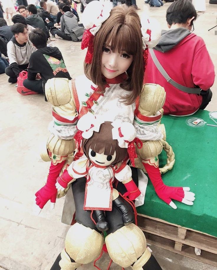 a doll sitting on top of a green bench in front of people wearing red and white outfits