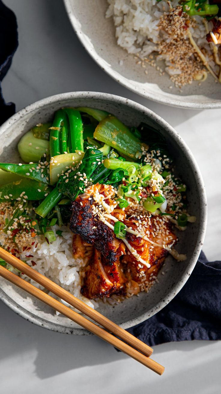 two bowls filled with food and chopsticks on top of a white tablecloth