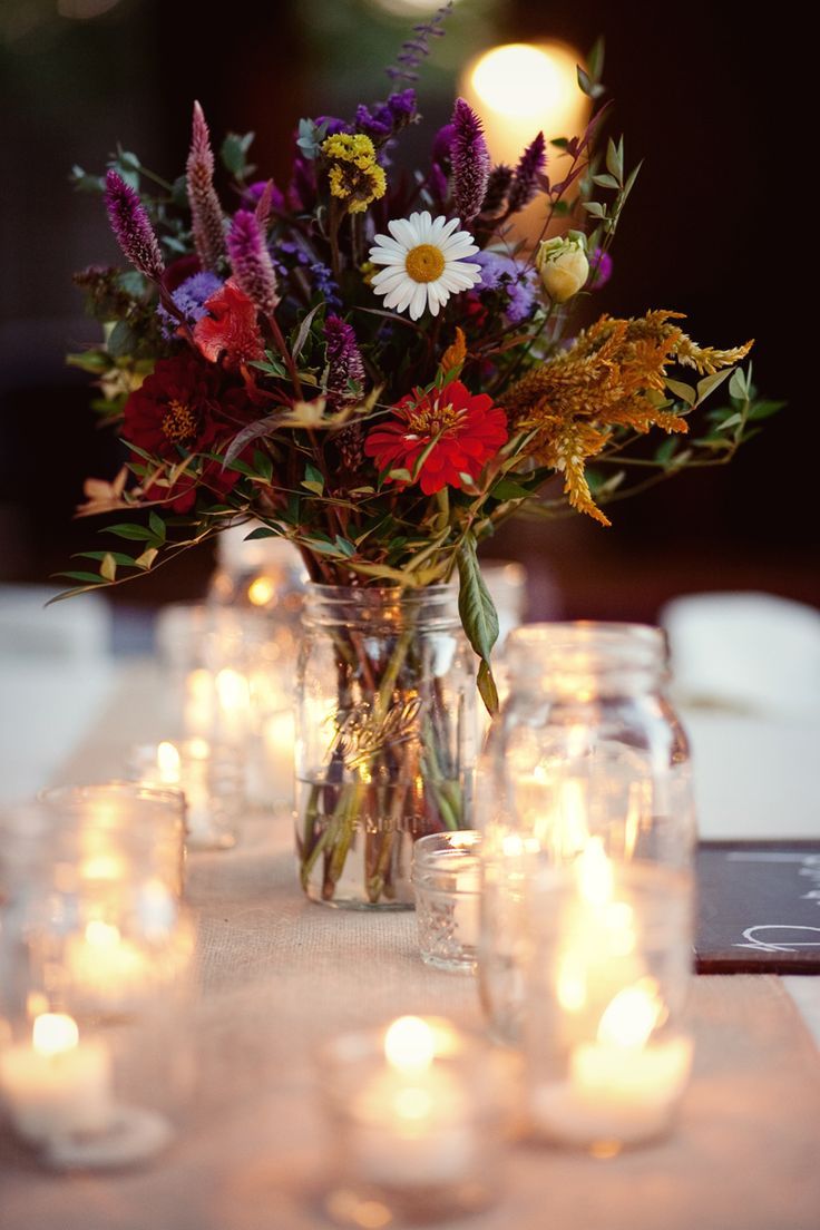 a vase filled with lots of flowers sitting on top of a table covered in candles