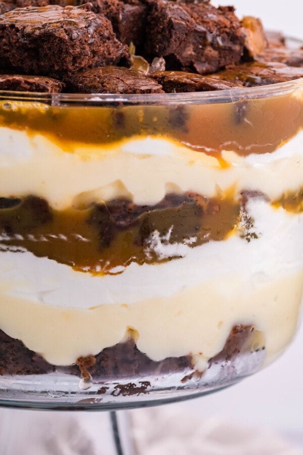 a layered dessert in a glass dish with brownies and white frosting on top