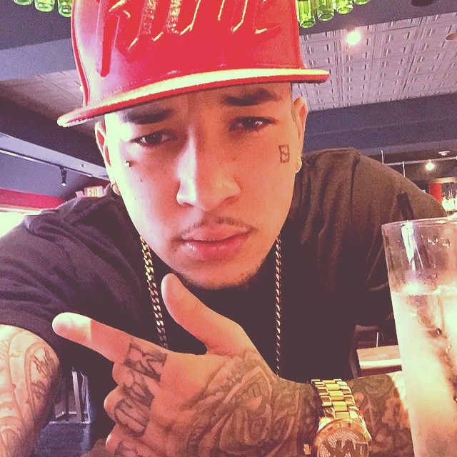 a man with tattoos and a red hat pointing to the side while sitting at a table