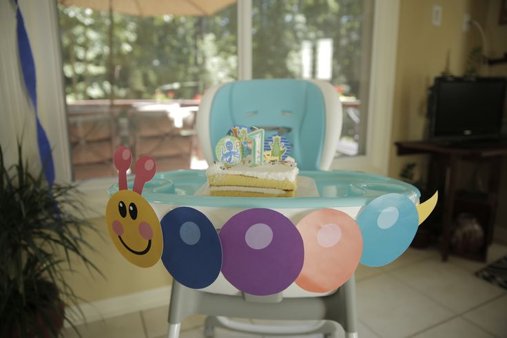 a birthday cake sitting on top of a blue high chair in front of a window