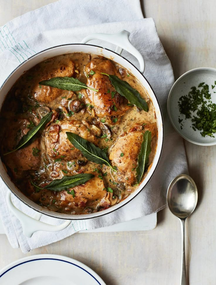 a white pot filled with chicken and green beans on top of a table next to two plates