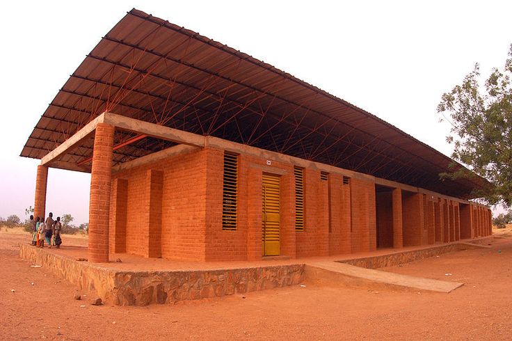 people are standing in front of a red brick building with a large roof over it