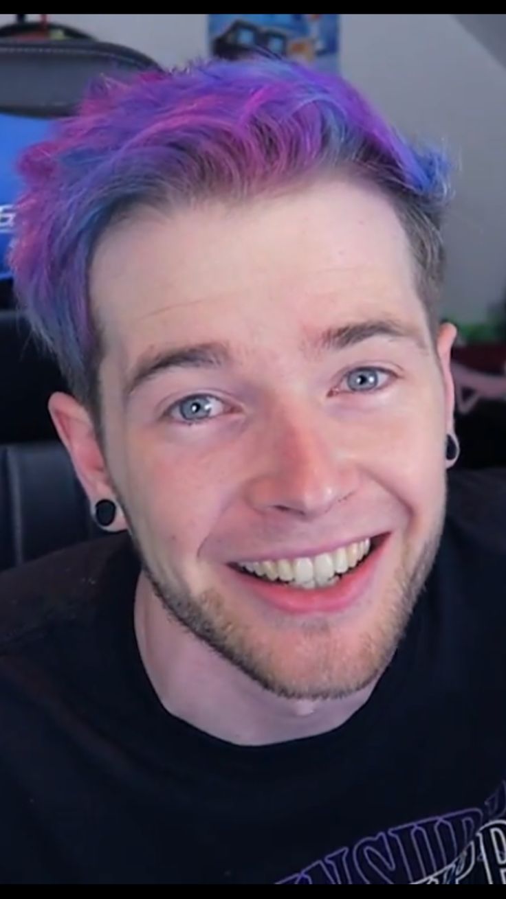 a man with purple hair and piercings smiles at the camera