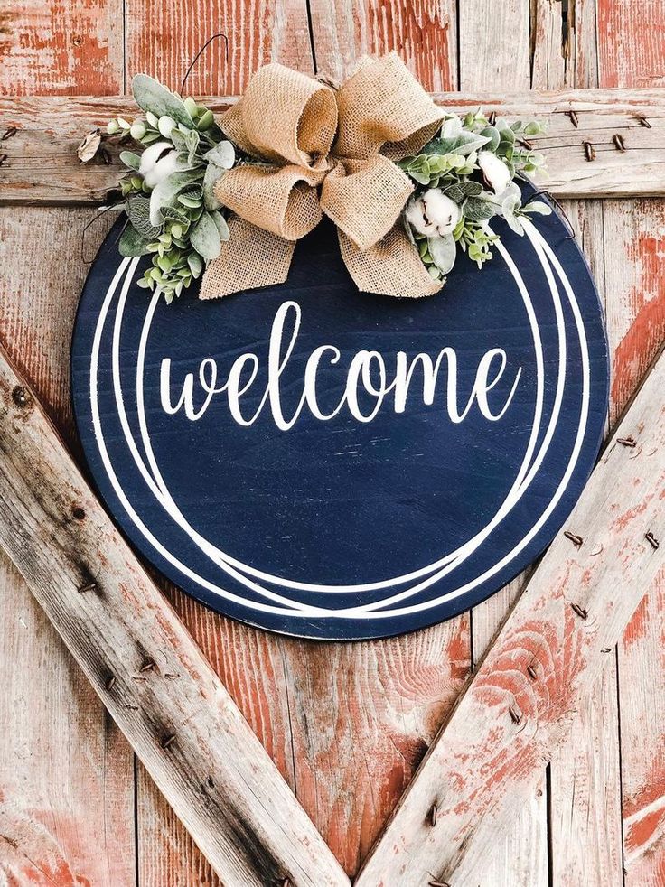 a blue welcome sign hanging on the side of a wooden door with a burluck bow