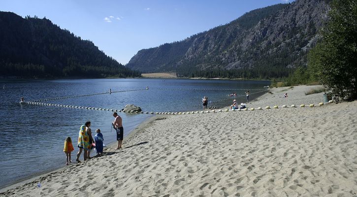 several people are standing on the beach by the water and mountains in the background,