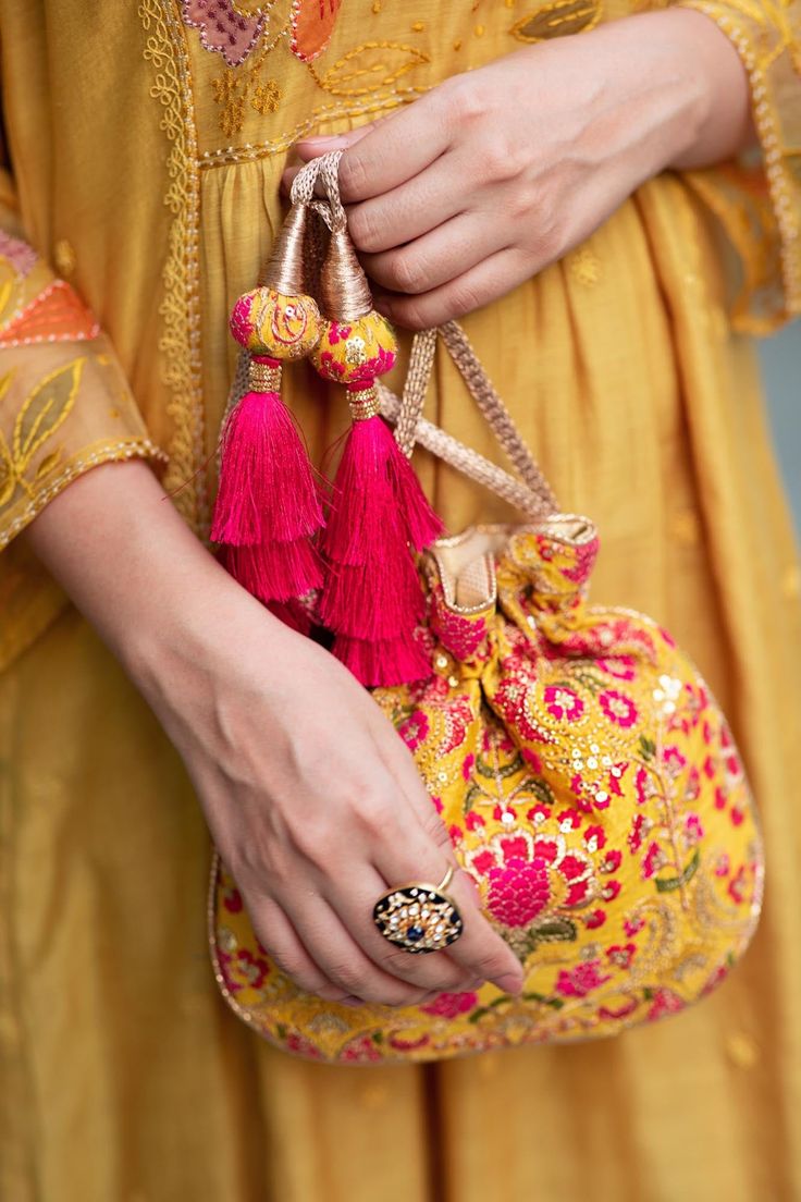 "Our Alanna potli is detailed with thread and zari and sequin embroidery on soft silk. Pair this with a vibrant pink ensemble and watch it stand out as a statement accessory! Colour: Mustard with pink Embroidered front and back. Dimensions (LxB): 8.5\"×9.5\" Handle drop: 5\" Material : Embroidered silk, gold tissue, poly satin lining, woven gold thread drawstrings and silk thread tassle detailing." Traditional Pink Shoulder Bag For Party, Festive Pink Handcrafted Shoulder Bag, Festive Multicolor Embroidered Handwork Clutch, Multicolor Embroidery Handwork Potli Bag, Pink Embroidered Shoulder Bag For Festivals, Festive Party Clutch With Resham Embroidery, Traditional Party Fabric With Gota Work, Festive Pink Shoulder Bag For Wedding, Pink Bag For Festive Party