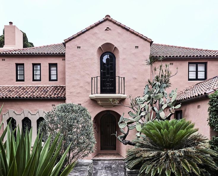 a large pink house with lots of plants in front of it and a black door